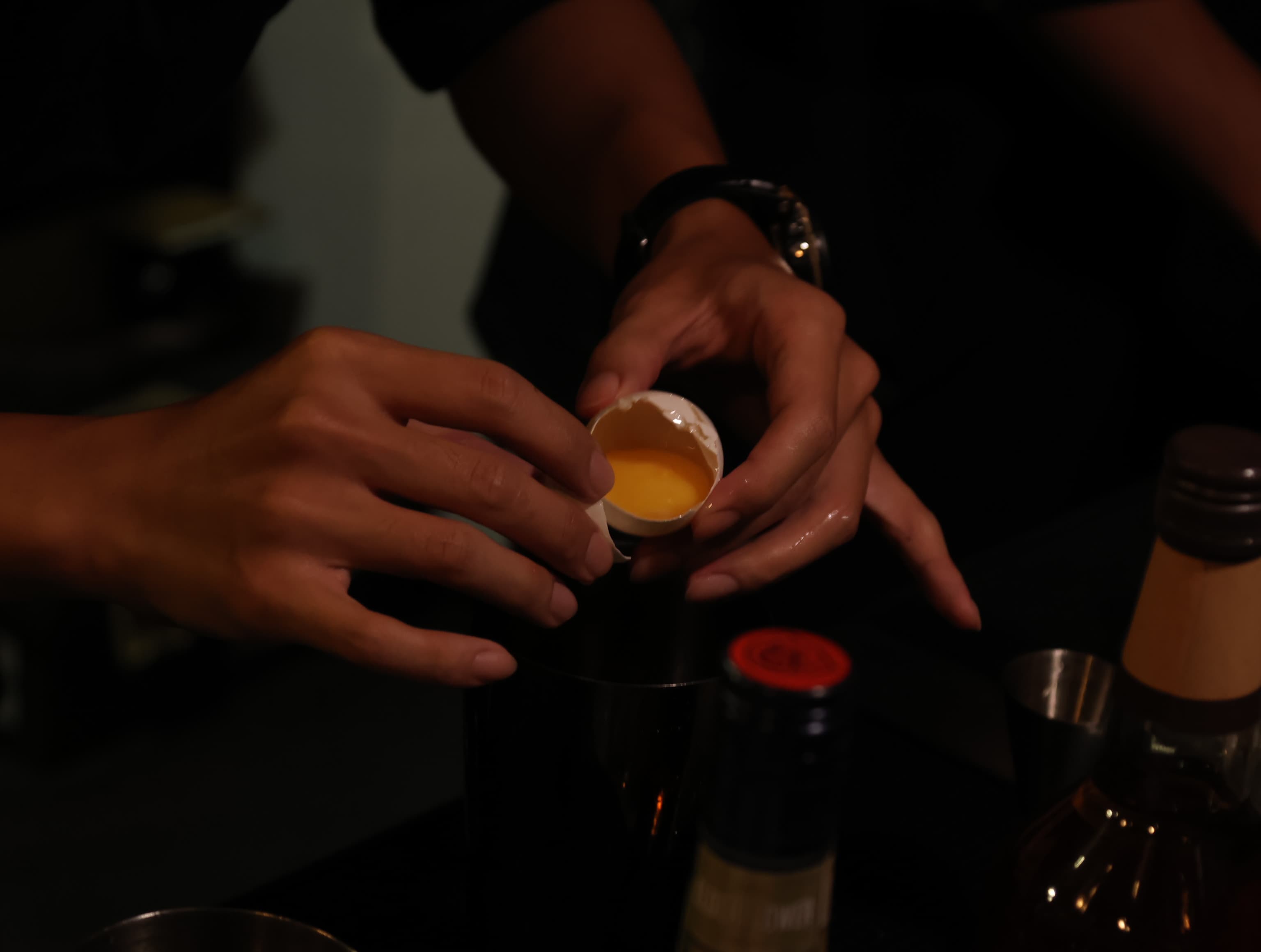 Bartender cracking an egg into a cocktail shaker