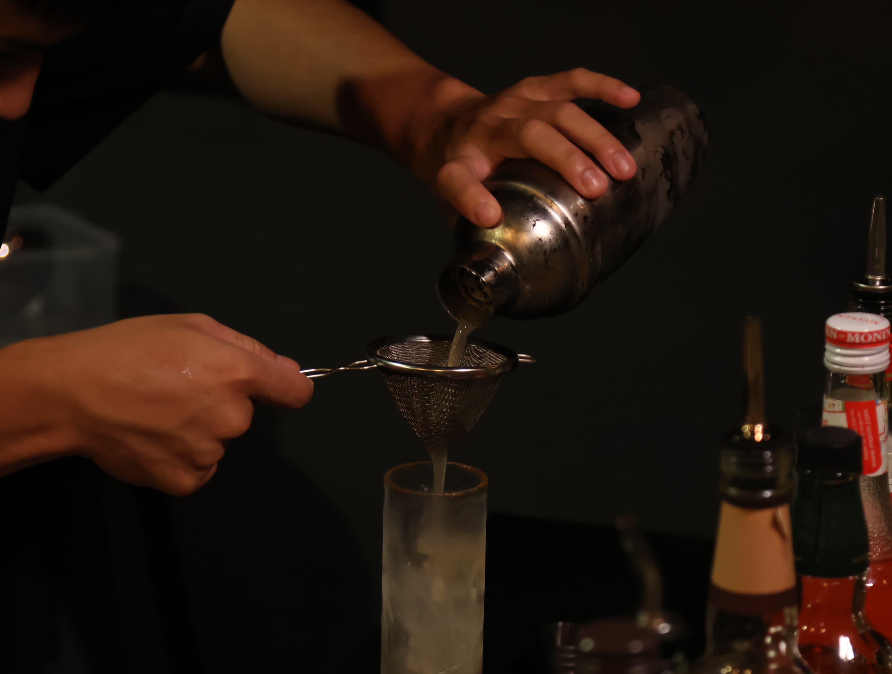 Bartender double-straining a cocktail